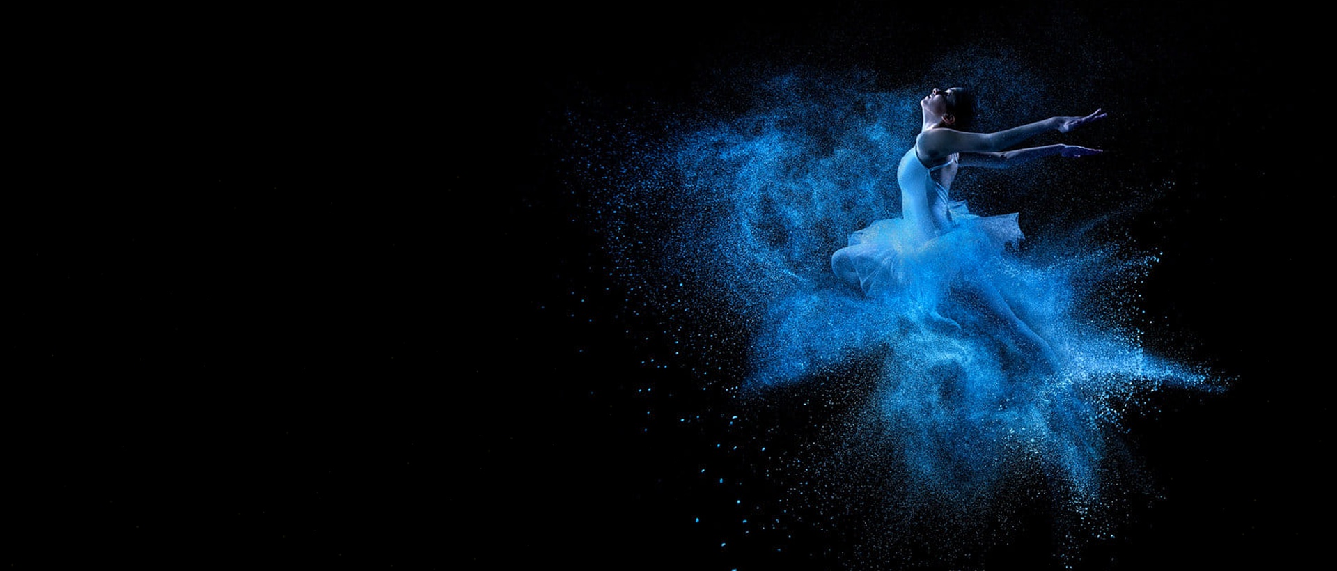 Dancer leaping in blue powder against a dark background